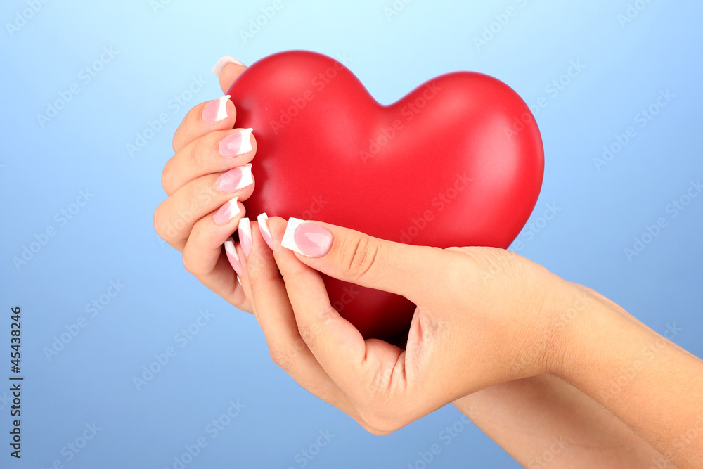 Red heart in woman's hands, on blue background close-up