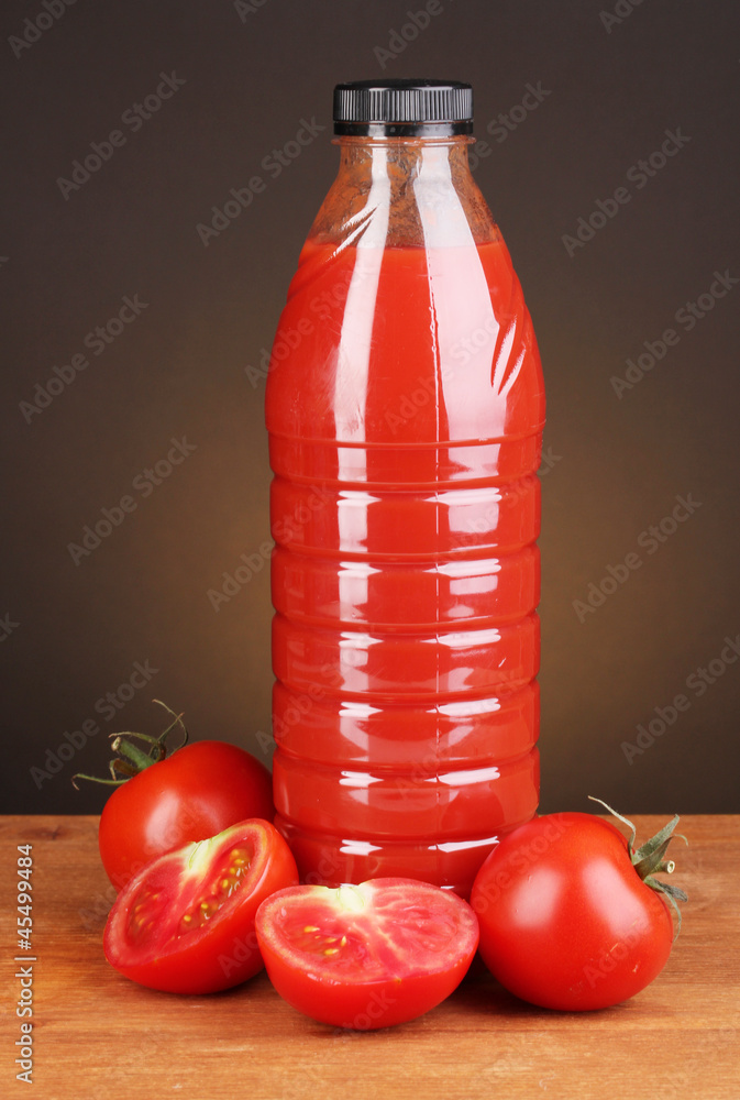 Tomato juice in bottle on wooden table on brown background