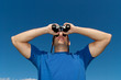 © chamillew - young man looking with binoculars, blue sky as background