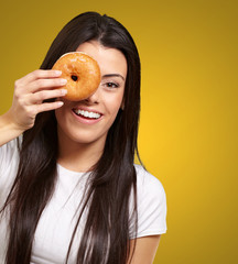 Wall Mural - portrait of young woman looking through a donut over orange