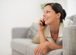 © Alliance - Happy young woman laying on sofa and speaking cell phone