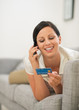 © Alliance - Happy woman on sofa holding credit card and speaking mobile