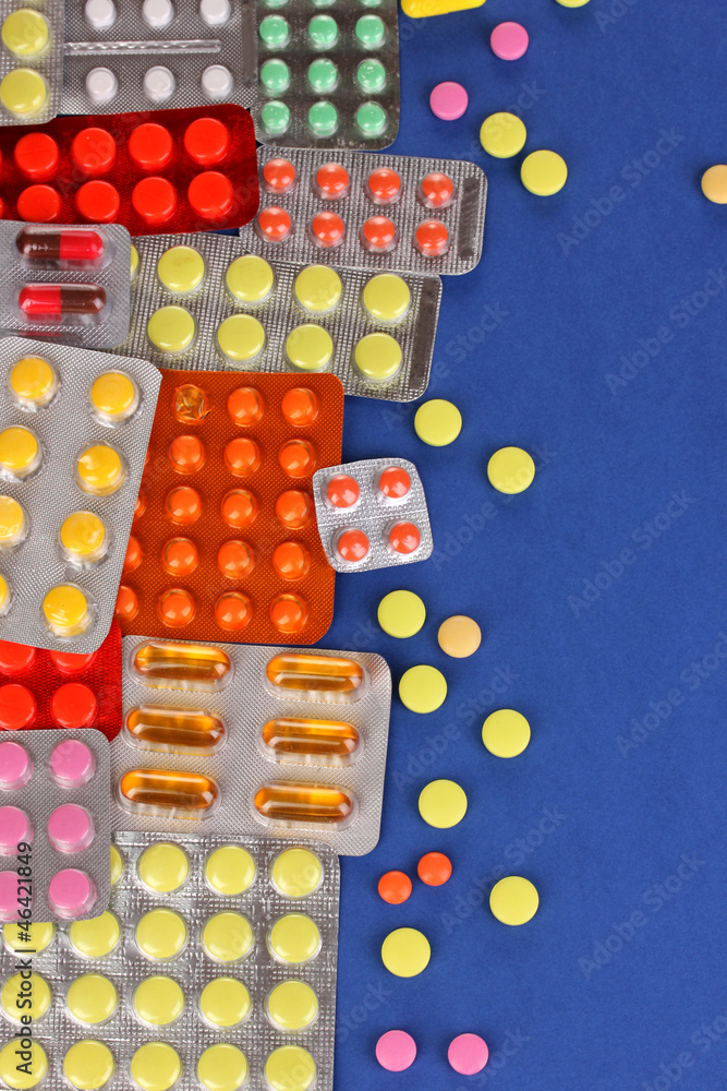 Capsules and pills packed in blisters on blue background