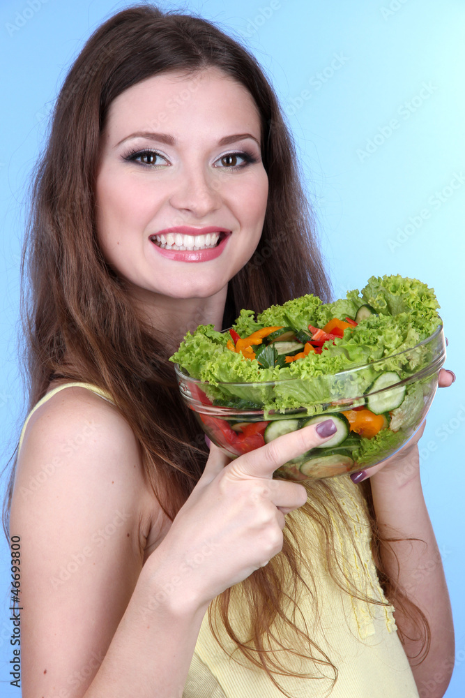 Beautiful woman with vegetable salad on blue background