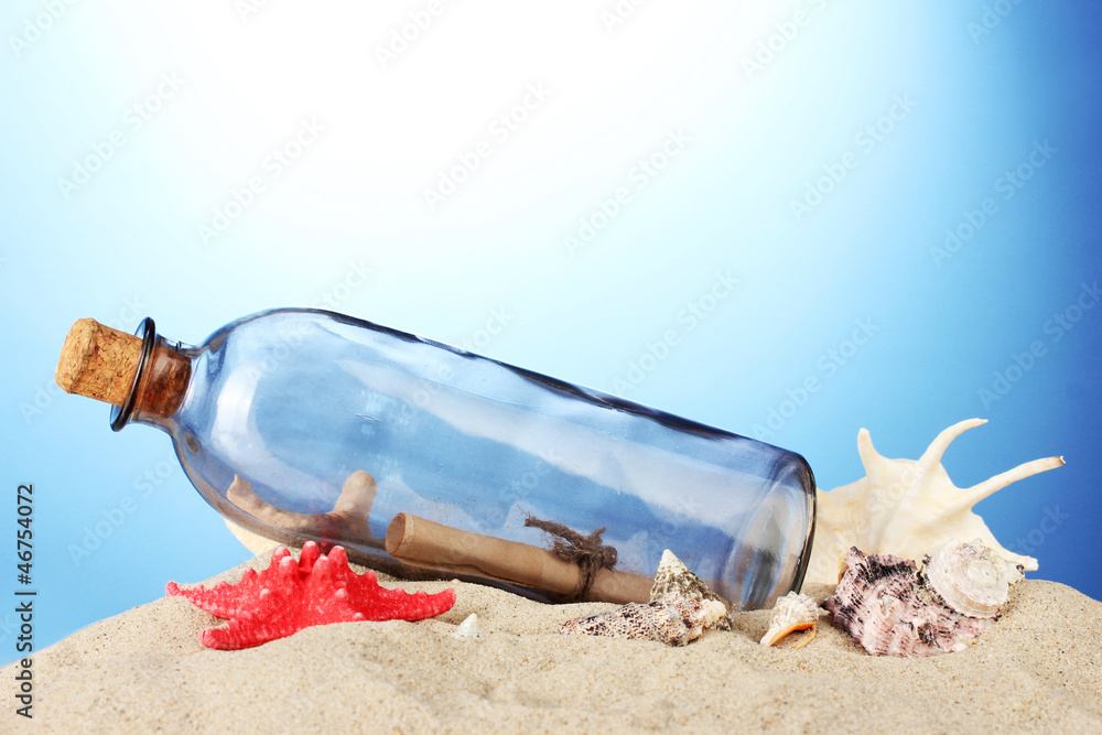 Glass bottle with note inside on sand, on blue background