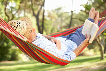 senior man relaxing in hammock with book