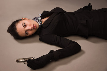 Wall Mural - Woman in a black suit with gun lying on the floor