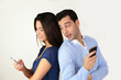 © goodluz - Couple standing back to back and using smartphone