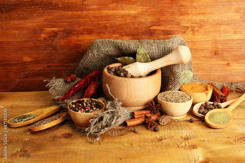 mortar, bowls and spoons with spices, on wooden background