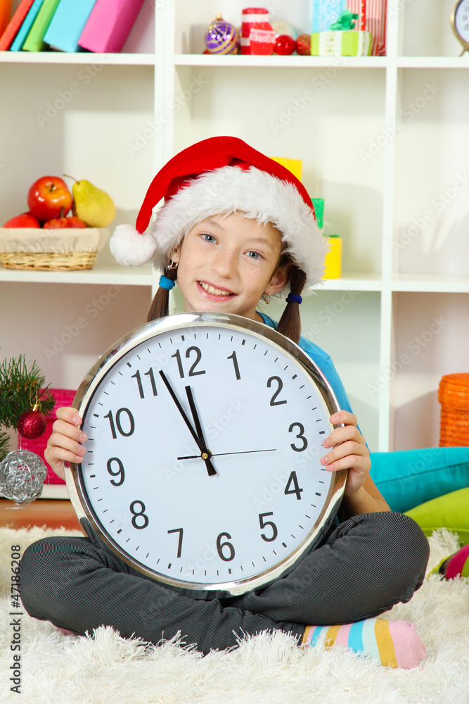 Little girl holding clock near christmas tree