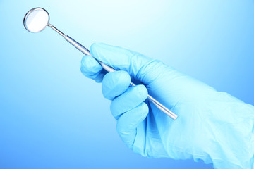 Hand in blue glove holding dental mirror on blue background