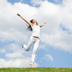 Pretty young woman jumping on green grass