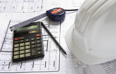 Hard hat, calculator, pencil and tape measure lying on blueprint