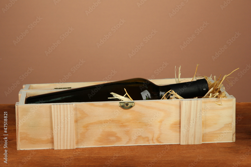 Wine bottle in wooden box on wooden table on brown background