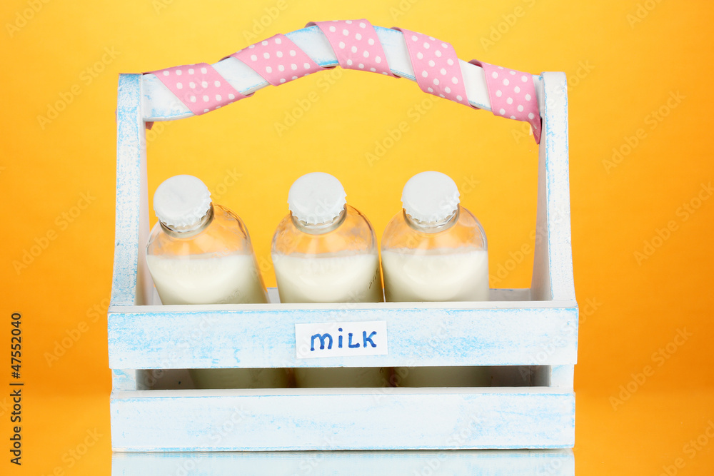Milk in bottles in wooden box on orange background