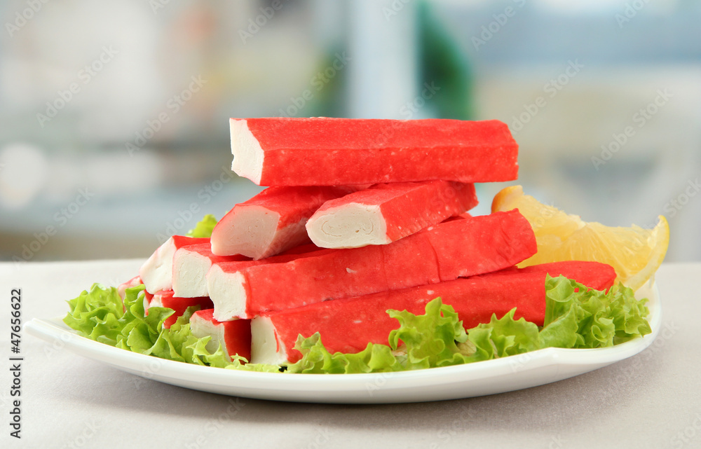 Crab sticks with lettuce leaves and lemon on plate, close up