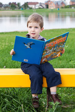 Милый мальчик в парке читает книгу