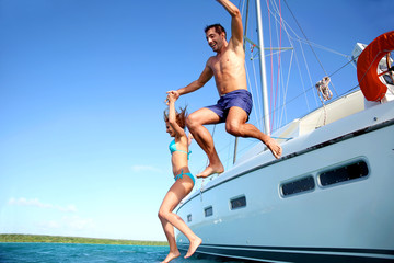 Young couple jumping in water from yacht