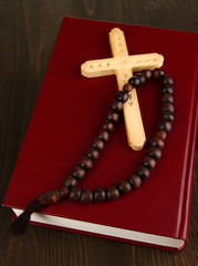 Bible, rosary and cross on wooden table close-up