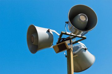 Three loudspeakers on a column against the blue sky