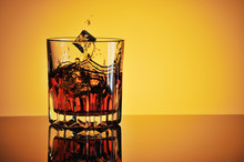 Glass Of Whisky With Ice Against Yellow Background