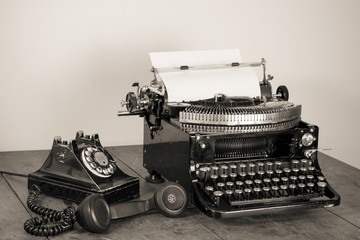 Vintage phone, old typewriter on table desaturated photo