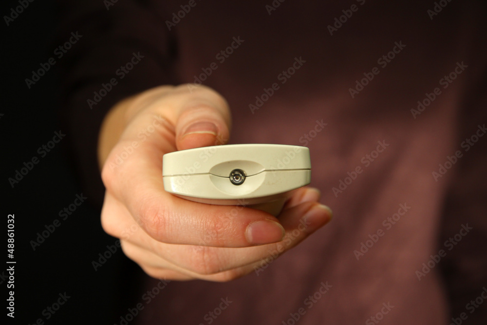 Woman hand holding a TV remote control, on dark background