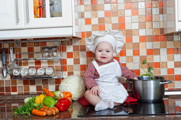 baby cook with vegetables sits on a kitchen table