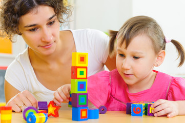 Young mother and little daughter playing with toy blocks