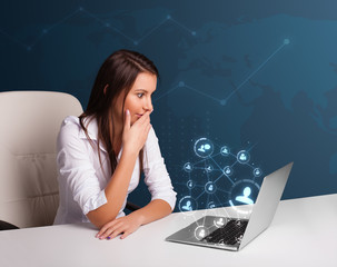 Young lady sitting at desk and typing on laptop with social netw