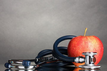 Medical stethoscope and red apple on grey