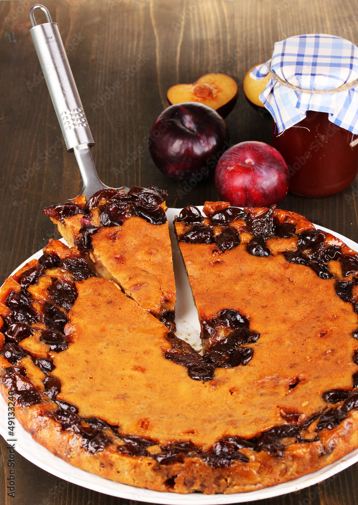 Tasty pie on plate with plums on wooden table