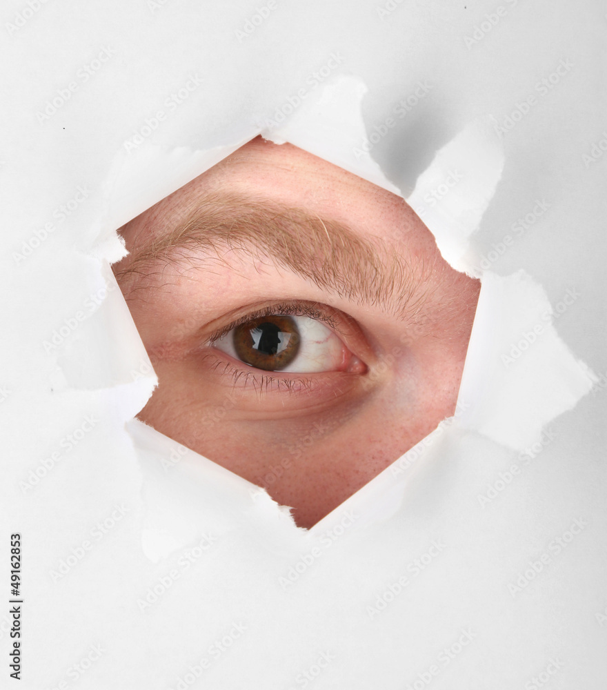 Man eye looking through hole in sheet of paper