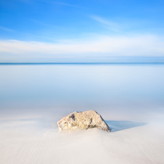 Wall Mural - Rock on a white sand beach and sea on horizon.