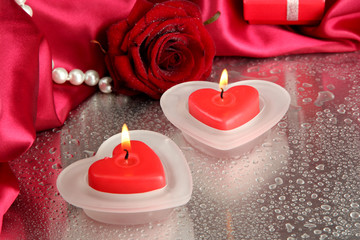 Beautiful candles, rose and red silk on grey wet background