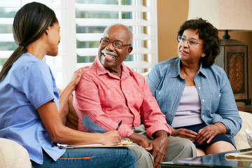 nurse making notes during home visit with senior couple