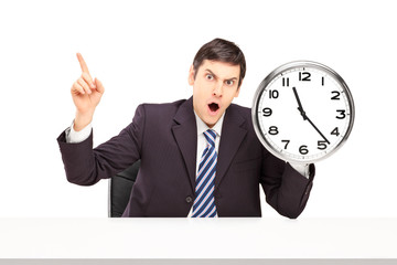 Wall Mural - Angry businessman sitting and holding a wall clock