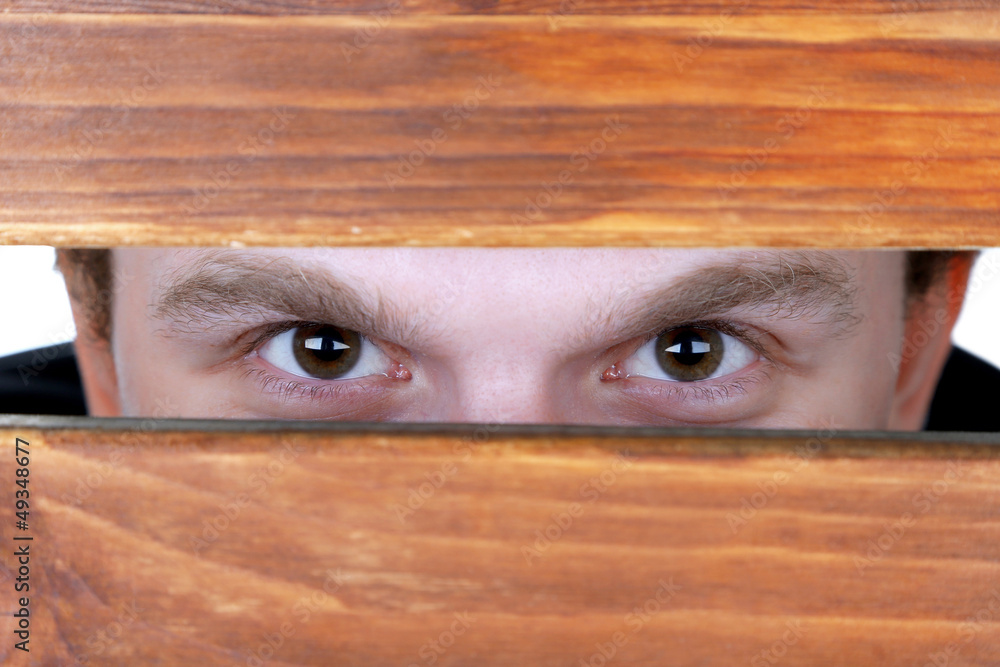 Man eyes looking through hole in wooden desk