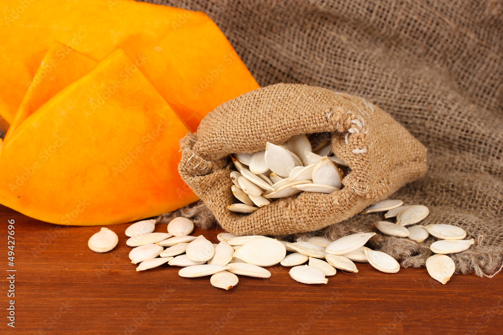 Pumpkin seeds in sack, on wooden background