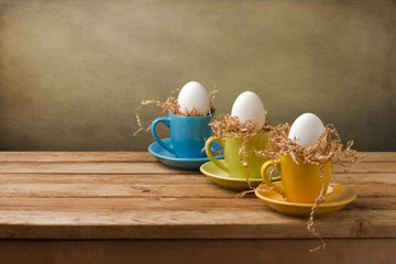 Wall Mural - Background with easter eggs in coffee cups on wooden table