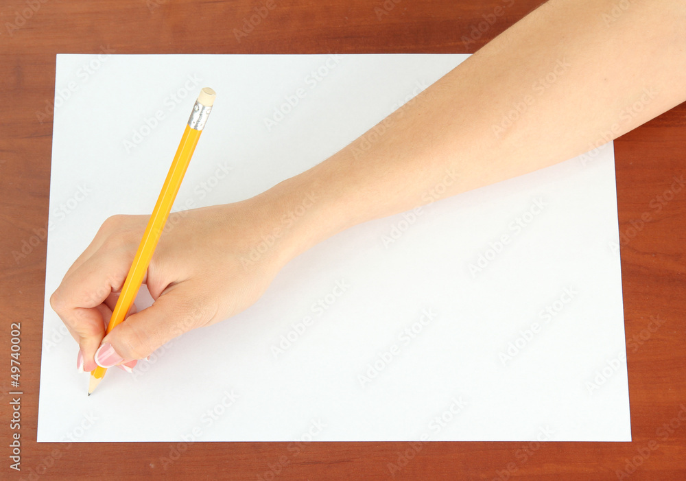 Hand with pencil on white paper, on wooden background