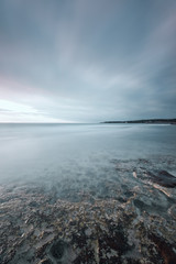 Wall Mural - Submerged rocks, ocean and cloudy sky on bay beach