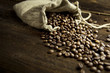 Burlap bag filled with coffee beans on dark wooden board