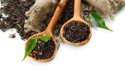 Dry tea with green leaves in wooden spoons, isolated on white