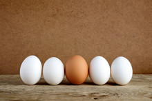 One Brown Egg Among White Eggs On Wooden Table