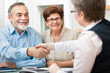 © Alexander Raths - senior couple smiling while shaking hand with financial advisor