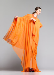 beautiful woman in long orange dress posing in the studio