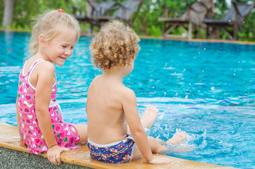 little girl and little boy sitting  in the swimming  pool