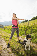 Caucasian Woman With Dog Stretching In Vineyard