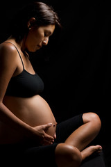 Pregnant Peruvian woman touching her belly against black backgro